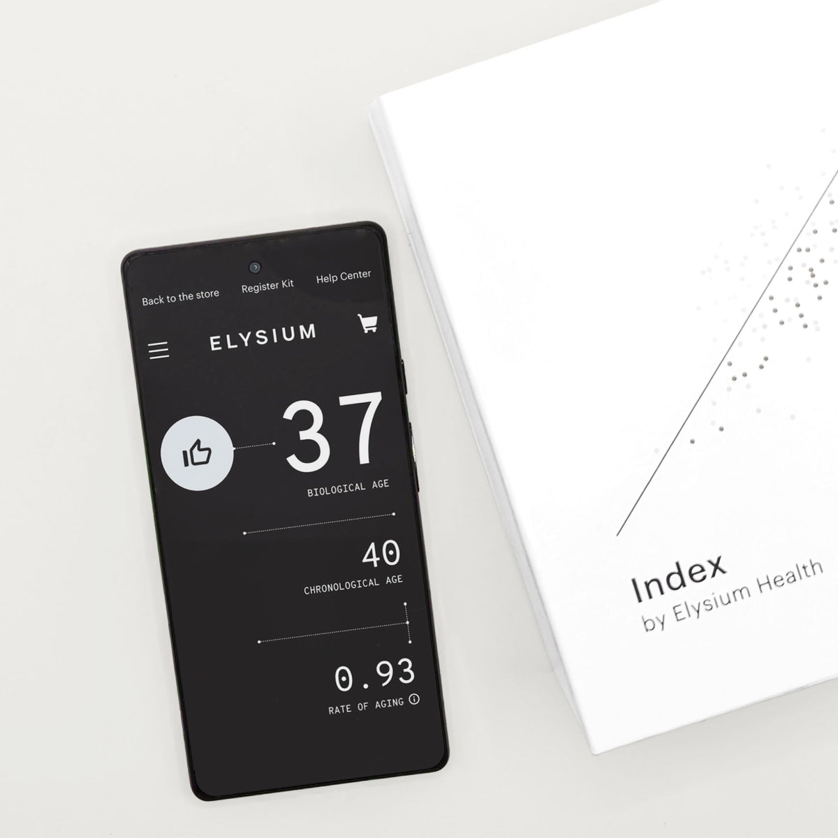 A black smartphone displaying the Elysium age-tracking app interface lies next to a white branded box labeled 'Index by Elysium Health' on a clean white background.