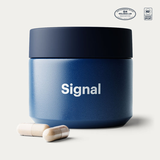 A dark blue textured jar with a black lid, featuring the word 'Signal' in white text on the front. Two beige capsules are placed in front of the jar on a light beige background.