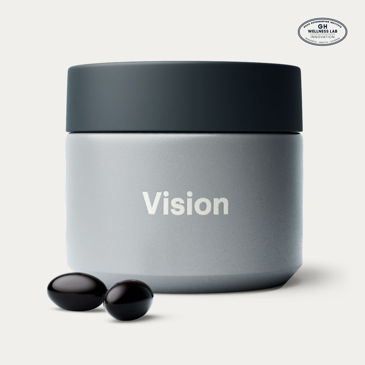 A matte gray cosmetic jar with a dark charcoal lid, featuring the word 'Vision' printed in white on the front. Two small black softgels are placed in front of the jar on a clean, light off-white background.